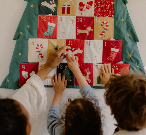 Children and a parent opening a pocket on a fabric Christmas tree Advent calendar to find the day’s family activity. - Mustela Australia - 1