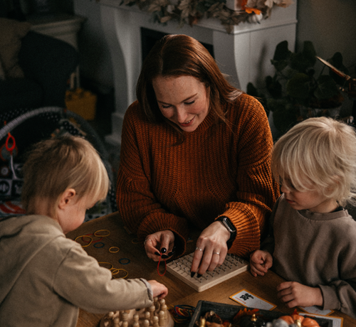 Mum playing a calm board game with two young children at a wooden table at home - Mustela Australia - 1